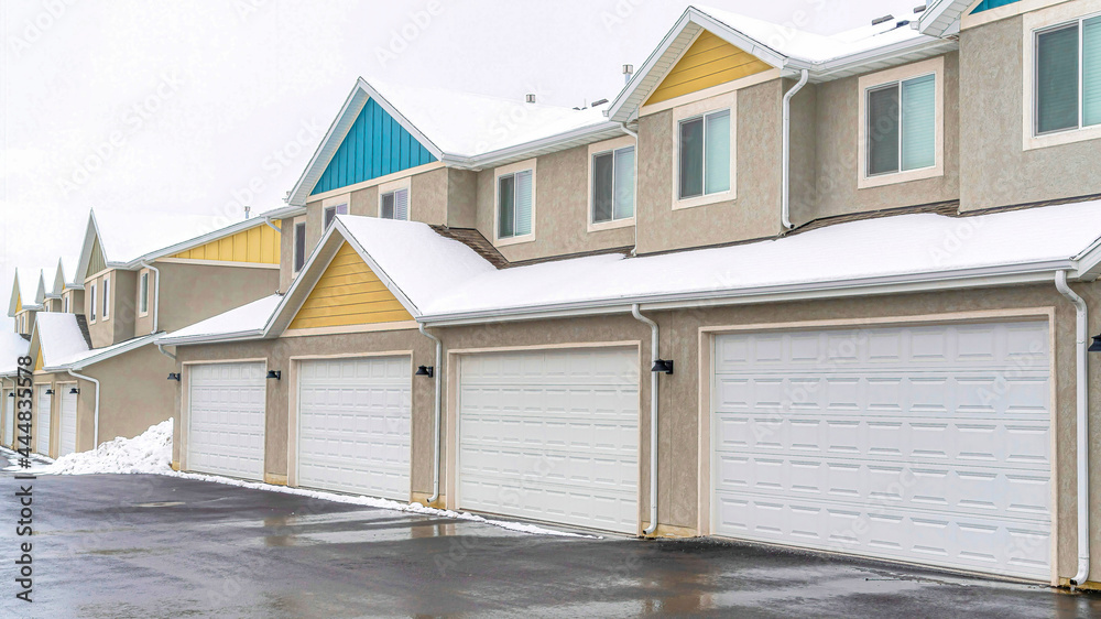 Pano Homes with white garage doors along wet and snowy road on a cloudy winter day Pano Homes with white garage doors along wet and snowy road on a cloudy winter day