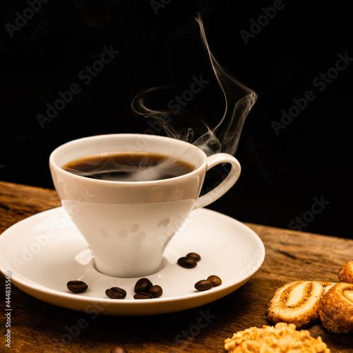 Bela foto de uma xícara de café quentinho, com grãos de café e biscoitos.