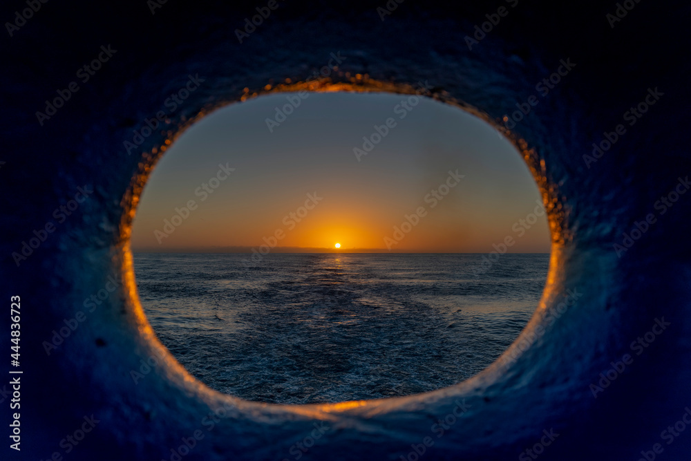 View to sunset throw porthole on the ship's stern. Beautiful seascape - waves and sky with clouds with beautiful lighting. Golden hour. View to sunset throw porthole on the ship's stern. Beautiful seascape - waves and sky with clouds with beautiful lighting. Golden hour.