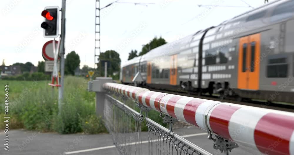 Selective focus view at red and white level crossing railway barrier which block the road and regional train move on the rail on countryside in Germany.	