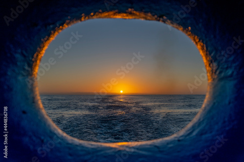 View to sunset throw porthole on the ship's stern. Beautiful seascape - waves and sky with clouds with beautiful lighting. Golden hour.