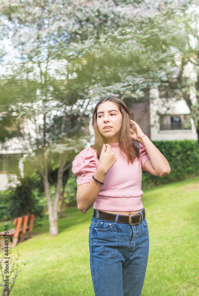 Outdoor portrait of a Latina teenage girl adjusting her straight hair with her hands in pink blouse and jeans Outdoor portrait of a Latina teenage girl adjusting her straight hair with her hands in pink blouse and jeans