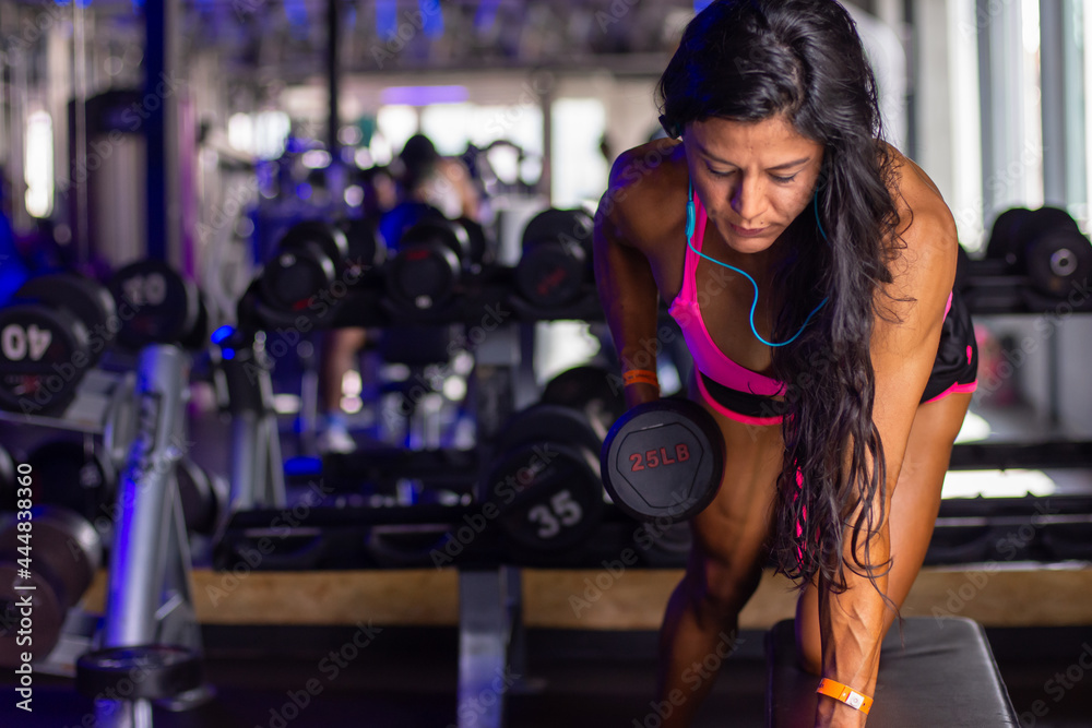 Mid age muscular woman lifting dumbbells in the gym