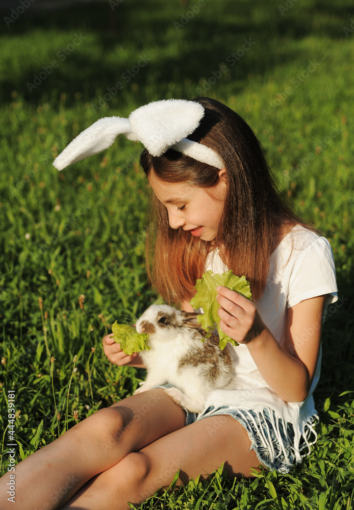 A little girl feeds a rabbit with cabbage leaves outdoors. Rabbit as a symbol of Easter. Good treatment of the child with the animal. A little girl feeds a rabbit with cabbage leaves outdoors. Rabbit as a symbol of Easter. Good treatment of the child with the animal.