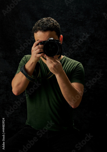 retrato de joven fotografo sosteniendo una camara  en un fondo negro con textura
