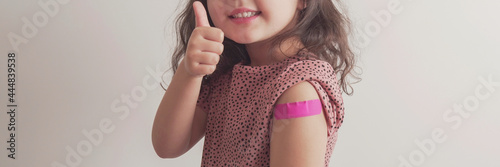 Foto Young  girl giving thumb up and showing her arm with pink bandage after got vacc