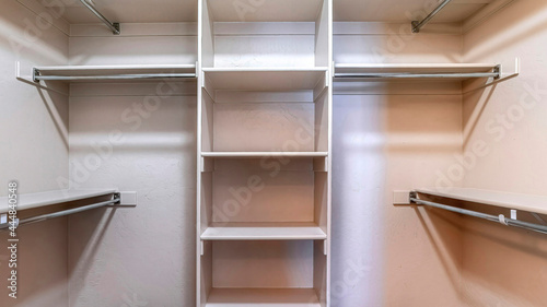 Pano Walk in closet with empty storage shelves for clothes built against white wall