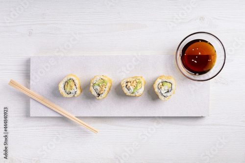 details of a white plate with sushi rolls, container of soy sauce and some wooden chopsticks, food in studio, delicious traditional dish