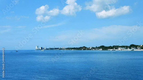 Distant view across beautiful blue water of the bay toward the waterfront of San Miguel de Cozumel under a clear blue sky with small fluffy clouds photo