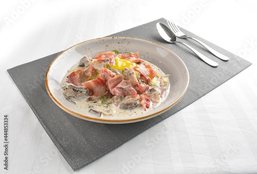 carbonara pasta with bacon, ham and half boiled egg in creamy cheese white sauce in white background western halal menu