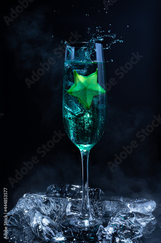 Cold blue cocktail with a star fruit garish on black background.