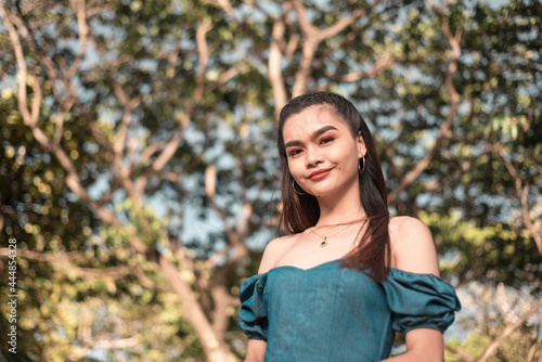 A classy and gorgeous young asian woman in a teal off shoulder top posing in the park during a beautiful day.