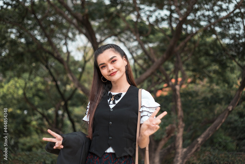 A elegant young woman in student uniform makes the peace sign in a cute way. Portrait of a beautiful teenager outdoors. photo