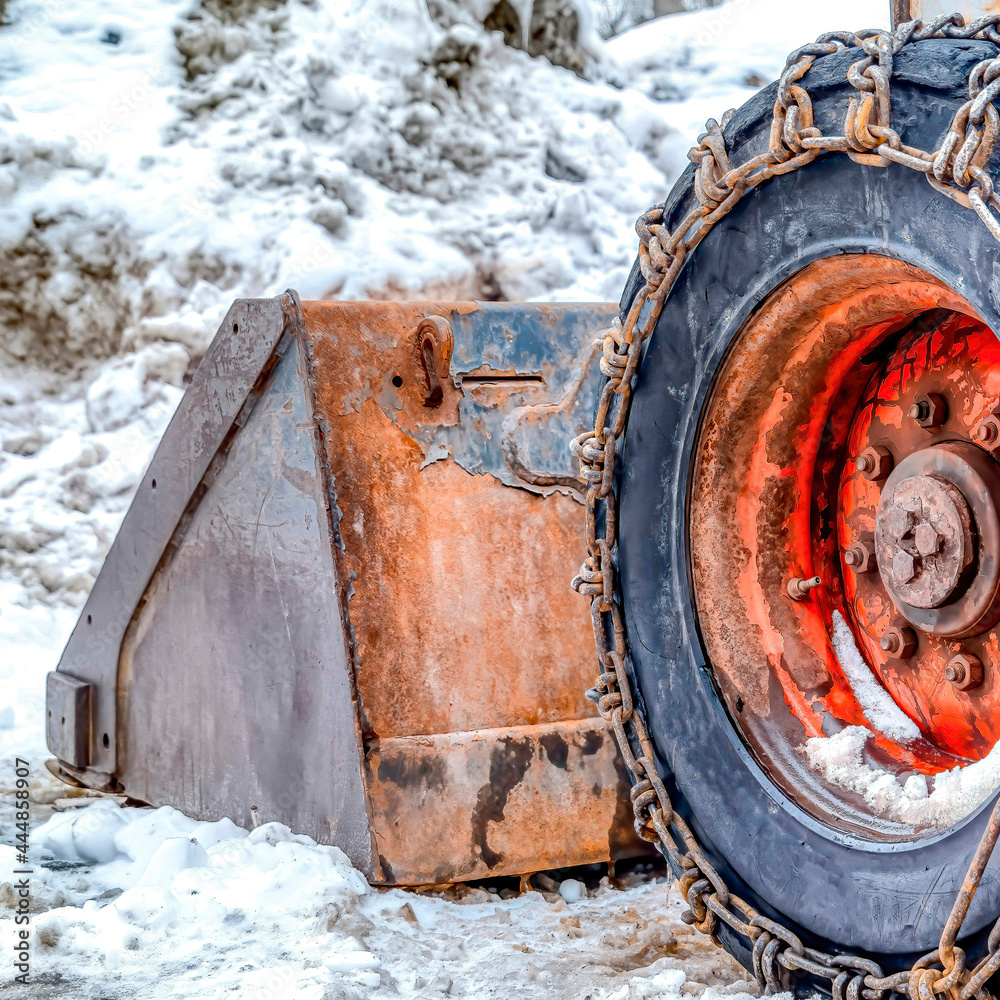Square Old snow bulldozer with rusty blade and black tires wrapped with chains