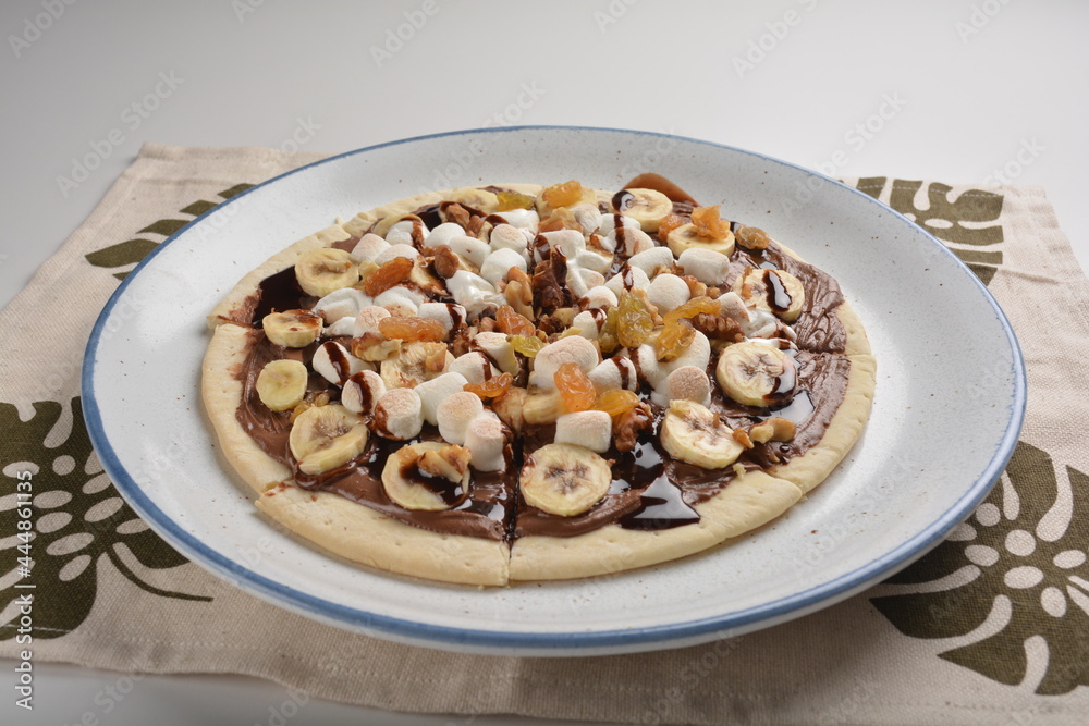 baked chocolate banana pizza with marshmallow and dry grape fruit dessert for kids in white background western halal menu baked chocolate banana pizza with marshmallow and dry grape fruit dessert for kids in white background western halal menu