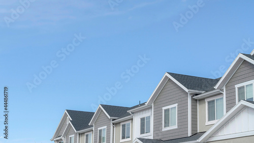 Pano Homes with gable roofs and gray exterior walls against blue sky in the suburbs