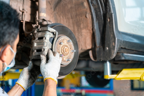 car mechanic examining car wheel brake disc and shoes of lifted automobile at auto repair service center