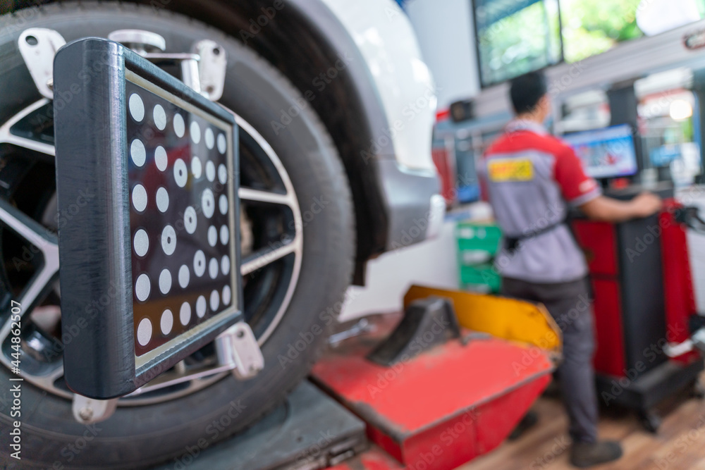 Car wheel balancer calibrate with laser reflector attach on each tire to center driving adjust. Balancing tire wheel machine at car repair service center.