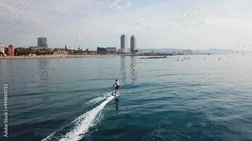 Aerial follow shot of fast surfer riding electric surfboard in front of iconic Barcelona skyline on a sunny day photo