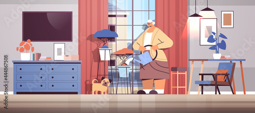 elderly woman watering flowers from watering can senior housewife taking care of house plants living room interior