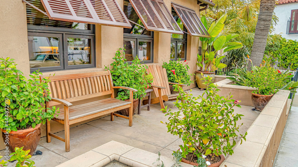 Pano Relaxing patio of house with wooden chair and bench against windows with awning