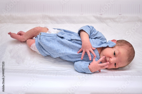 A newborn baby in blue clothes on a changing table with a Moro reflex photo