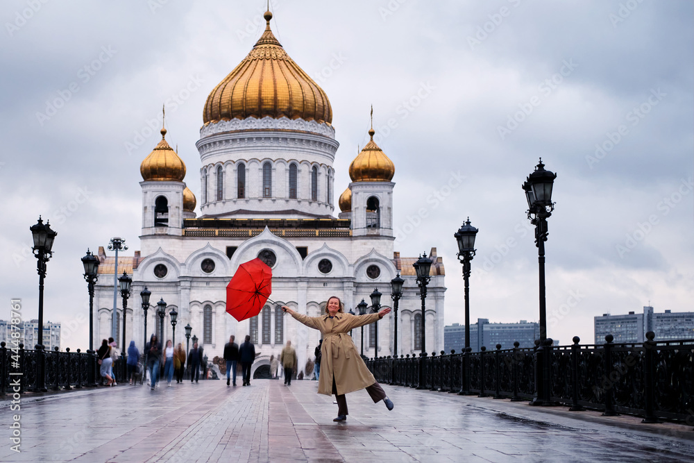 A happy woman with a red umbrella dances at the Cathedral of Christ the Saviour