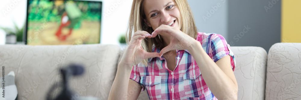 Smiling woman shows her heart to camera on tripod