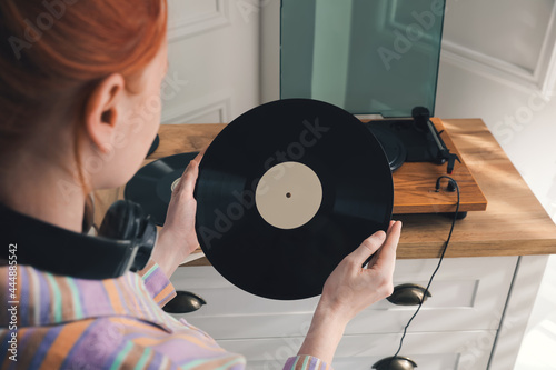 Young woman with vinyl disc near turntable at home