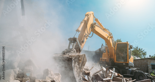 Destruction of old house by excavator. Bucket of excavator breaks concrete structure.