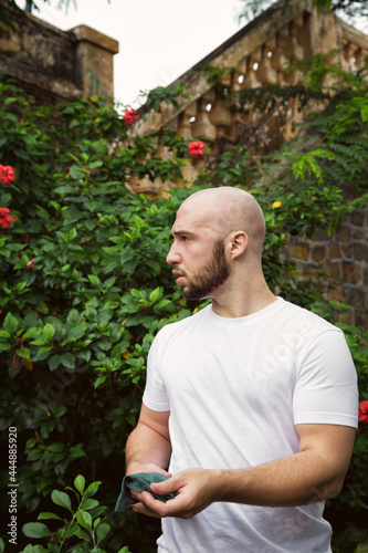 Serious, concerned man working in a park full of blooming trees. Young Caucasian male farmer in a green summer garden