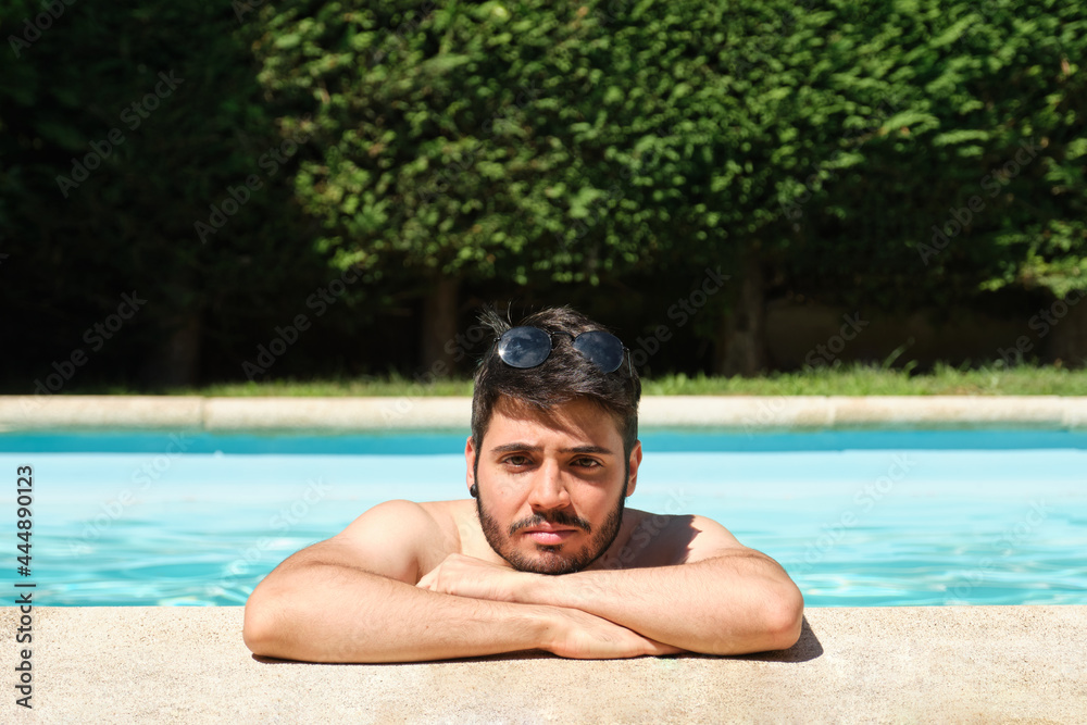 Portrait of a young man with sunglasses on his head, in a swimming pool looking at camera. Summer concept.