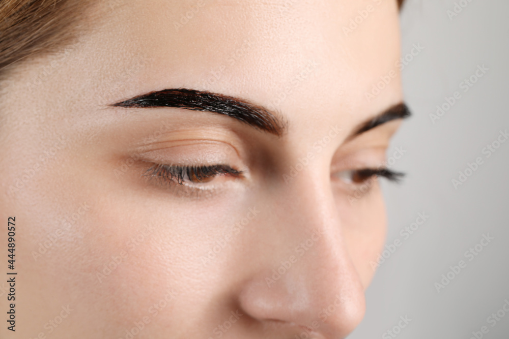 Woman during eyebrow tinting procedure on grey background, closeup Woman during eyebrow tinting procedure on grey background, closeup