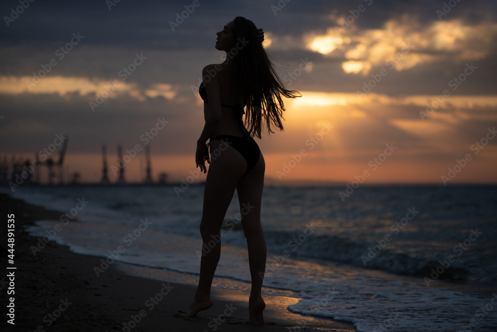Young girl walks on the sea coast at sunrise. Silhouette photography.