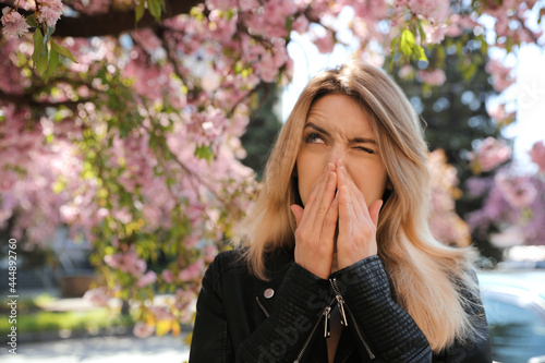 Woman suffering from seasonal pollen allergy near blossoming tree outdoors