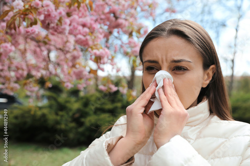 Woman suffering from seasonal pollen allergy near blossoming tree outdoors