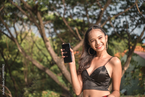Fotografi A spunky young teenage woman holds her cellphone up while outdoors