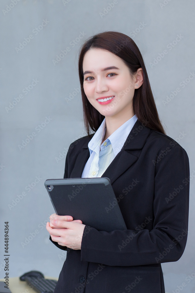 Asian professional working woman in a black suit holds tablet in her hands and smiles in office room. Asian professional working woman in a black suit holds tablet in her hands and smiles in office room.