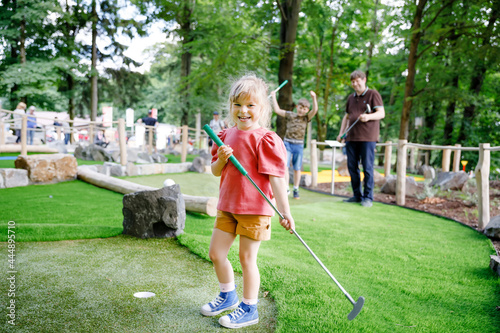 Cute preschool girl playing mini golf with family. Happy toddler child having fun with outdoor activity. Summer sport for children and adults, outdoors. Family vacations or resort. photo