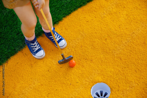 Cute preschool girl playing mini golf with family. Happy toddler child having fun with outdoor activity. Summer sport for children and adults, outdoors. Family vacations or resort. photo