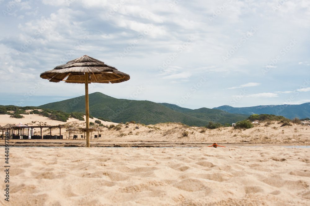 Fototapeta premium beach with wicker umbrella and mountains on background