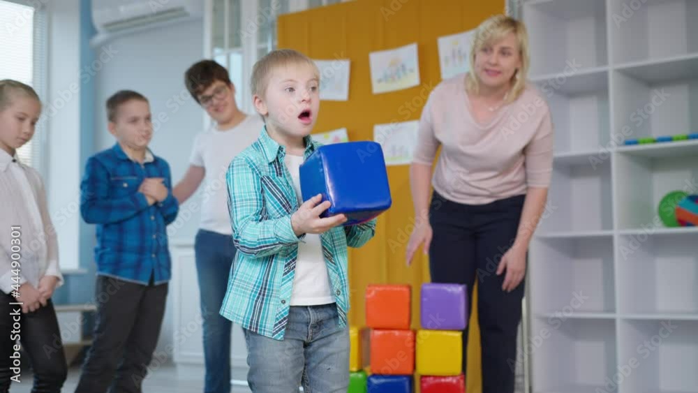 boy with down syndrome plays educational games with children and passing colored blocks to each other in an inclusive classroom