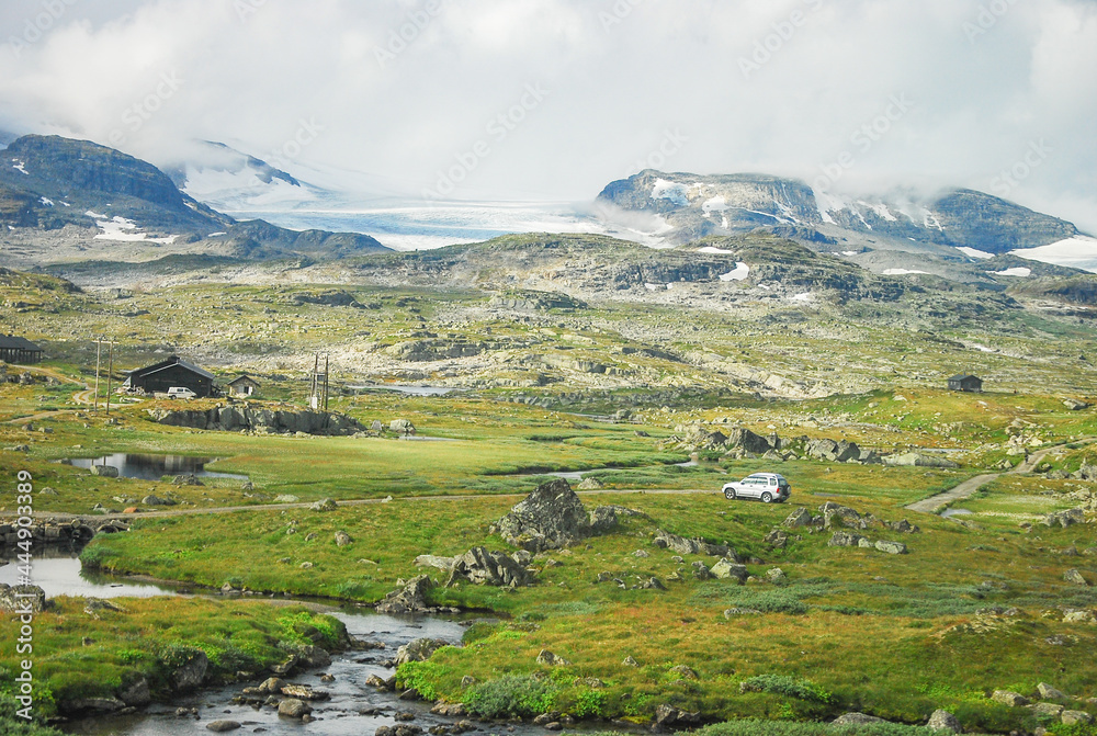 Panorama view of the scenic alpine meadow of Norway with glacier, stream, cottage house and a car
