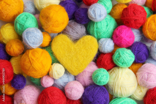 Colorful background of multi-colored yarn for knitting, crocheting,in the middle of a yellow woolen heart. The concept of handmade, needlework, sale in specialized stores. Top view. Flatlаy. Copyspacе