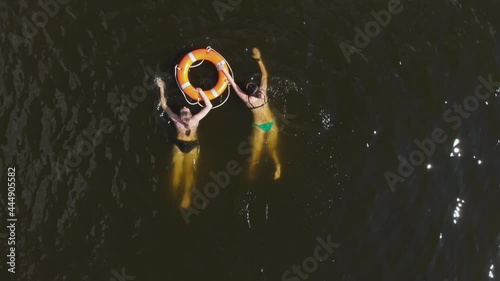 Two young caucasian women swim in the dark muddy water using life buoy. Water safety skills. Top angle aerial