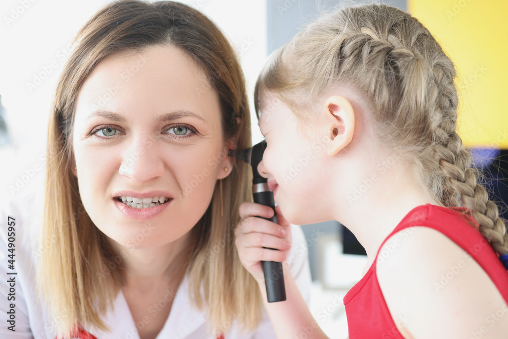 Little girl examines ear with otoscope to woman doctor Little girl examines ear with otoscope to woman doctor