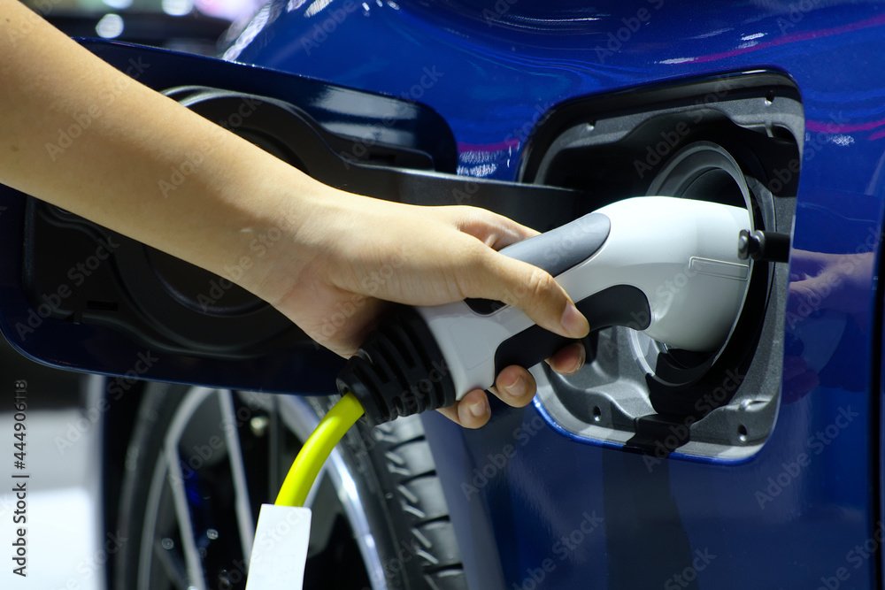 Close-up hand woman who holding electric charge machine for rechargeable battery with blue electric car, Zero Emission Vehicle (ZEV), Battery Electric Vehicle (BEV), Hybrid Electricity Vehicle (HEV)
