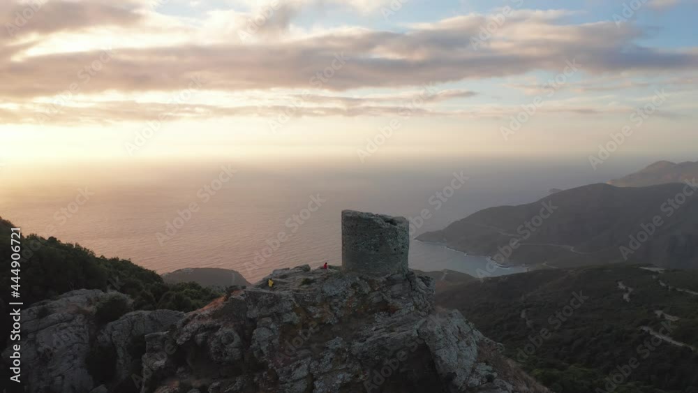 Beautiful panorama of aerial view of old and ancient building looking at the sea during sunset,green forest around.Two people on the top of mountain looking panorama,golden sea,clouds,mountain coast Beautiful panorama of aerial view of old and ancient building looking at the sea during sunset,green forest around.Two people on the top of mountain looking panorama,golden sea,clouds,mountain coast