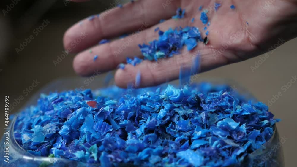 Female hand iterating blue plastic pieces lying in a transparent container 