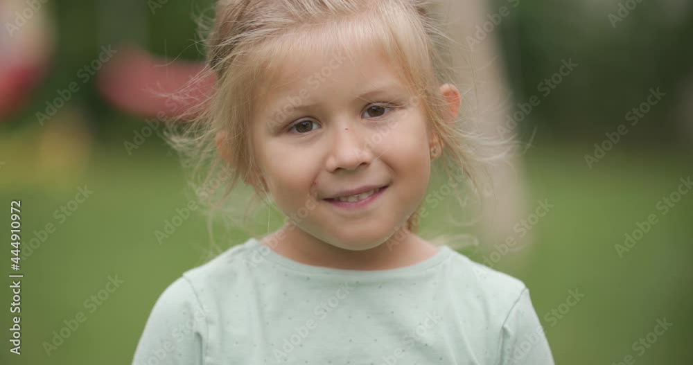 cute blonde kid with innocent eyes being timid, looking at camera and smiling while playing outside in backyard cute blonde kid with innocent eyes being timid, looking at camera and smiling while playing outside in backyard